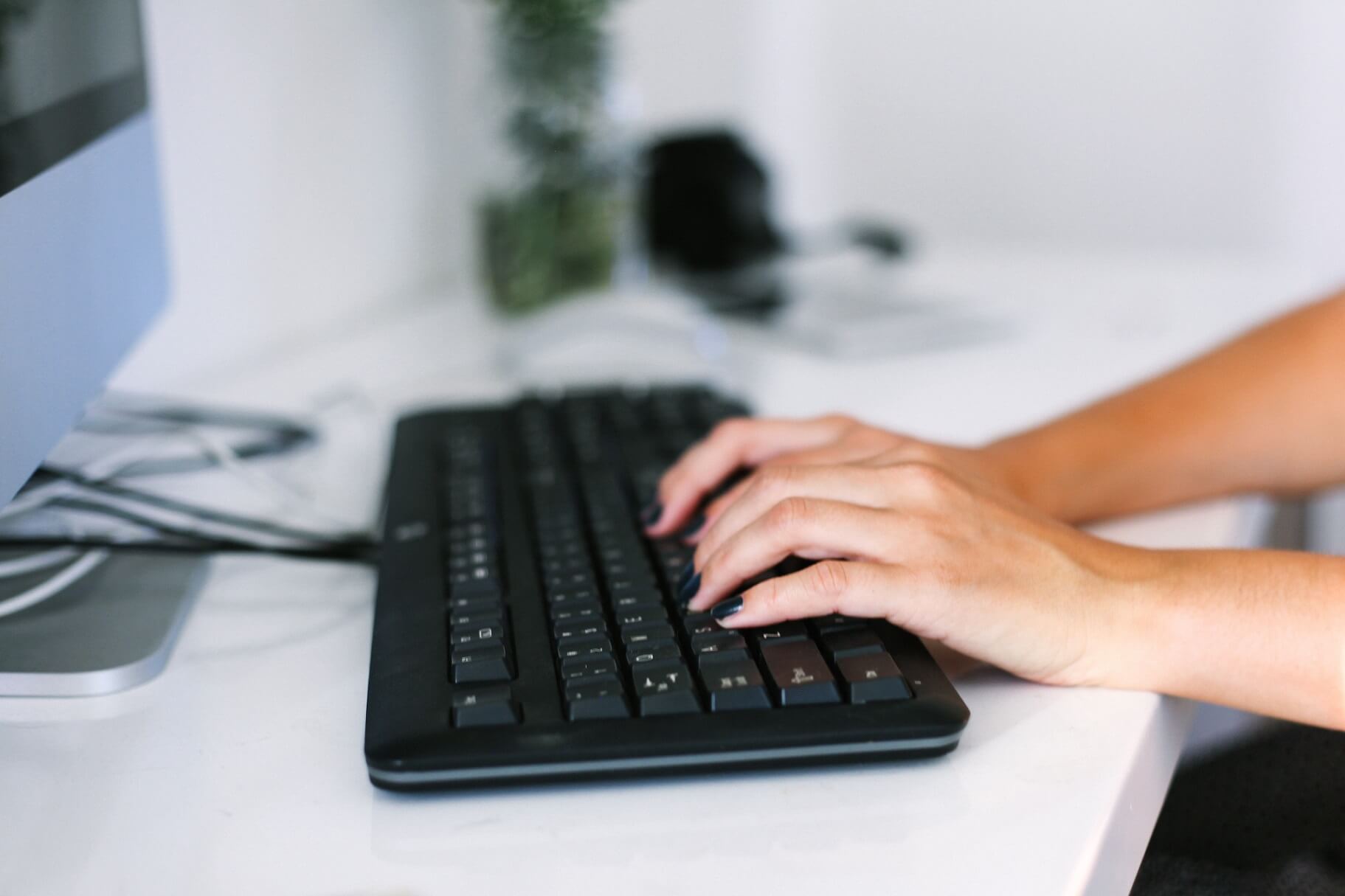 womans-hands-typing-on-keyboard-at-desk-working-in-JDKKPMP